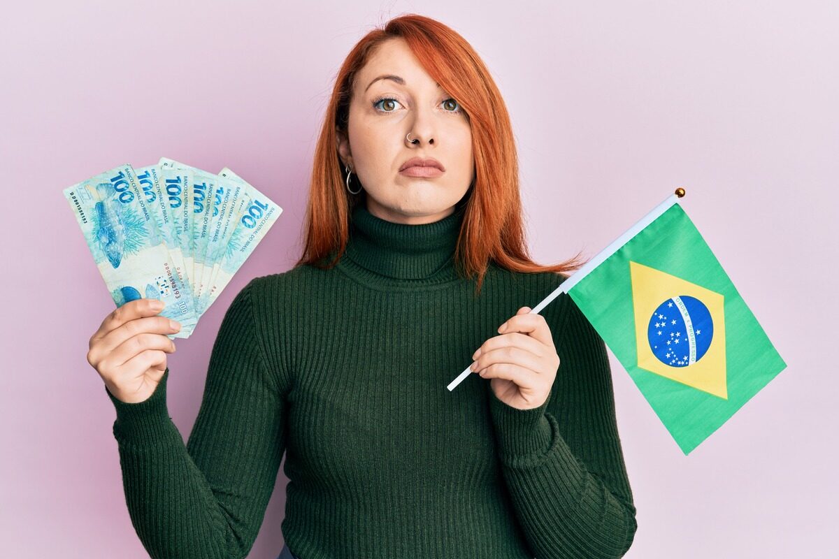 beautiful-redhead-woman-holding-100-brazilian-real-banknotes-brazil-flag-relaxed-with-serious-expression-face-simple-natural-looking-camera (1) (1)