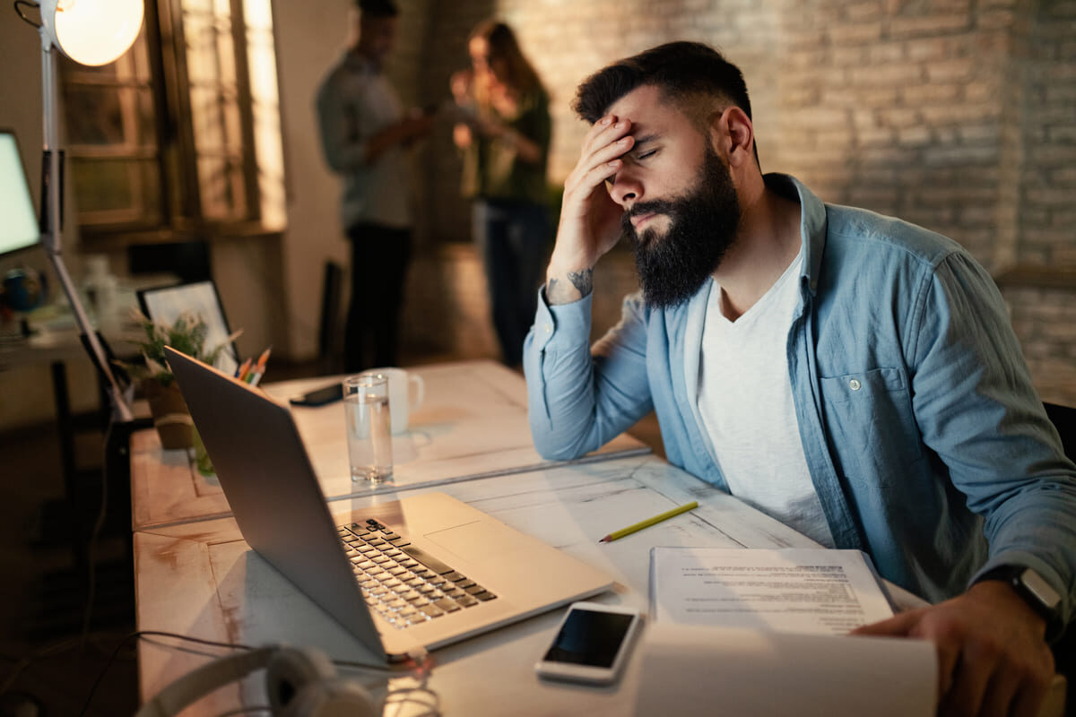 exhausted-businessman-holding-his-head-pain-while-working-late-office