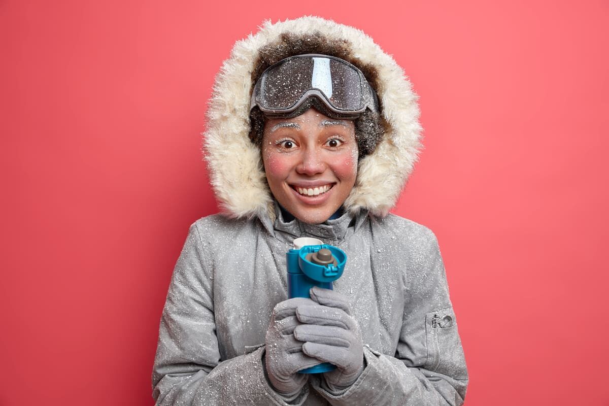 positive-woman-spends-time-outdoor-frosty-weather-drinks-hot-beverage-from-thermos-smiles-gladfully-dressed-outerwear