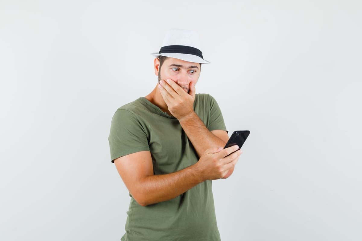 young-male-looking-mobile-phone-green-t-shirt-hat-looking-surprised